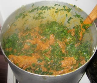 Stirring and mixing pot of Nigerian groundnut soup with vegetables